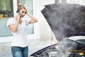 young woman talking on mobile phone in front of smokey car engine